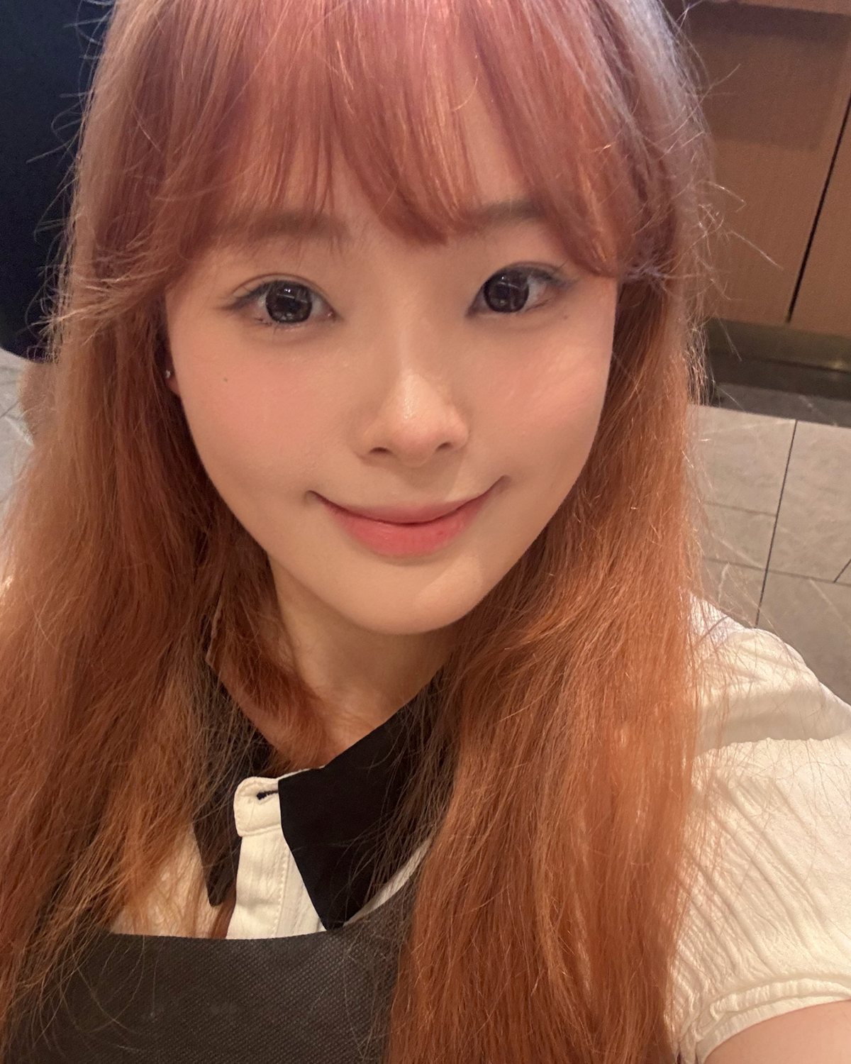 王宣懿 Diana 生活照:棕红色长发、齐刘海,微笑看向镜头,身穿白色上衣配深色背心裙,室内自拍